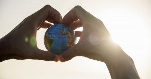 Die Erdkugel als Modell in den Händen eines Menschen, die zusammen ein Herz formen und die Erdkugel umschließen