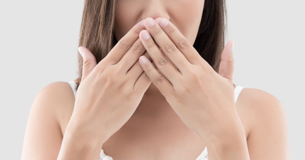 Eine Frau hält sich die Hand vor den Mund, da sie Mundgeruch hat und sich schämt