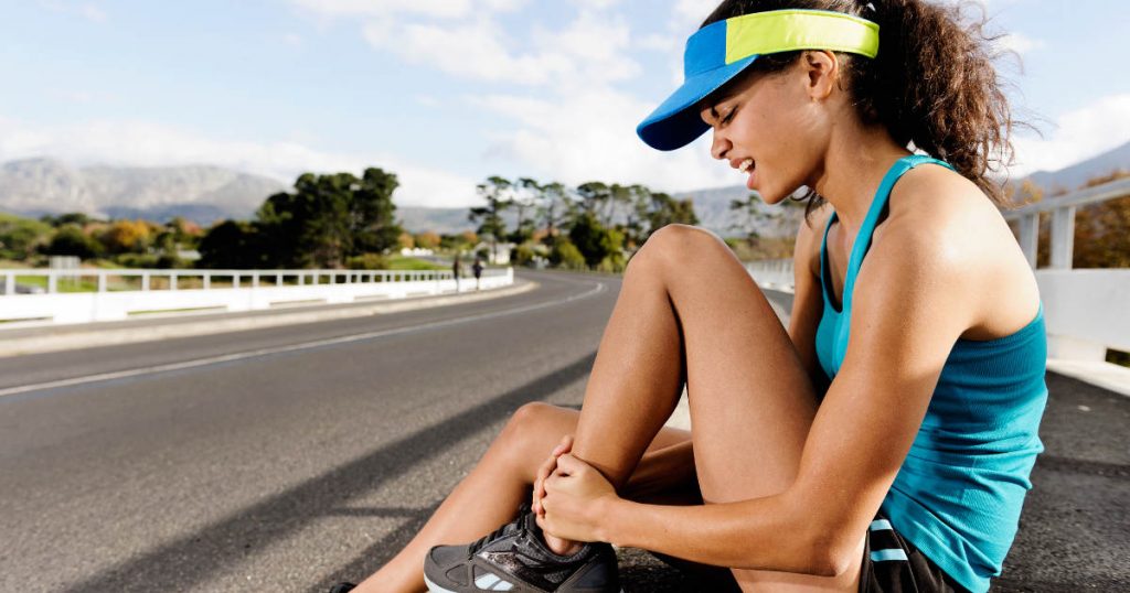 Eine Läuferin sitzt auf dem Boden und hält sich schmerzverzerrt ihren Fuß