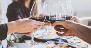 vier personen sitzen am Tisch und stoßen jeweils mit einem Glas Rotwein beim gemeinsamen Abendessen an