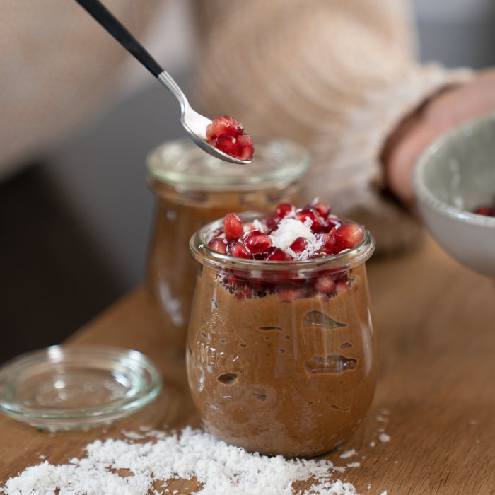 Schokopudding aus Süßkartoffel und Kakao ist in einem Weckglas. Als Topping Kokosflocken und Granatapfelkerne