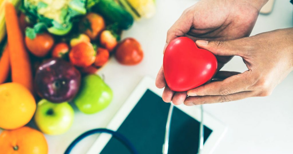 Abgebildet ist Obst und Gemüse,. Ein Arzt hält ein rotes Herz in der Hand, das symbolisiert, dass er sich für seine Patienten einsetzt.