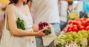 Eine junge Frau schaut sich auf dem Markt Obst und Gemüse an und kauft frische Produkte ein