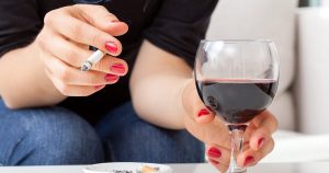 eine junge Frau sitzt auf dem Sofa, hält in der rechten Hand eine Zigarette und in der linken Hand ein Glas Rotwein