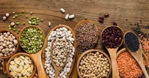 Verschiedene Bohnenarten und Linsen liegen auf kleinen Holzlöffeln und auf einem Tisch verteilt