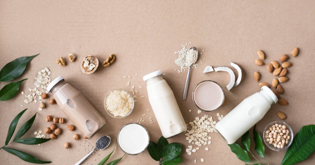 es liegen viele Nüsse, Getreidesorten und Glasflaschen mit jeweiliger Getreide-und Nussmilch auf einem Tisch