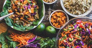 Viele verschiedene gesunde Lebensmittel sind auf einem Tisch abgebildet. Bunte Salate, Zitrusfrüchte und Hirse liegen nebeneinander.