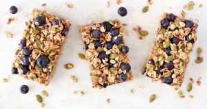 drei Haferriegel mit Blaubeeren und Kürbiskernen liegen nebeneinander.