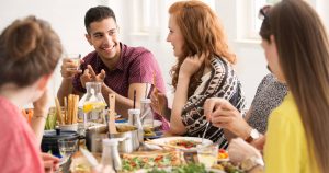 Freunde sitzen gemeinsam an einem großen Essenstisch und sitzen gemütlich beim Essen beieinander und sind fröhlich