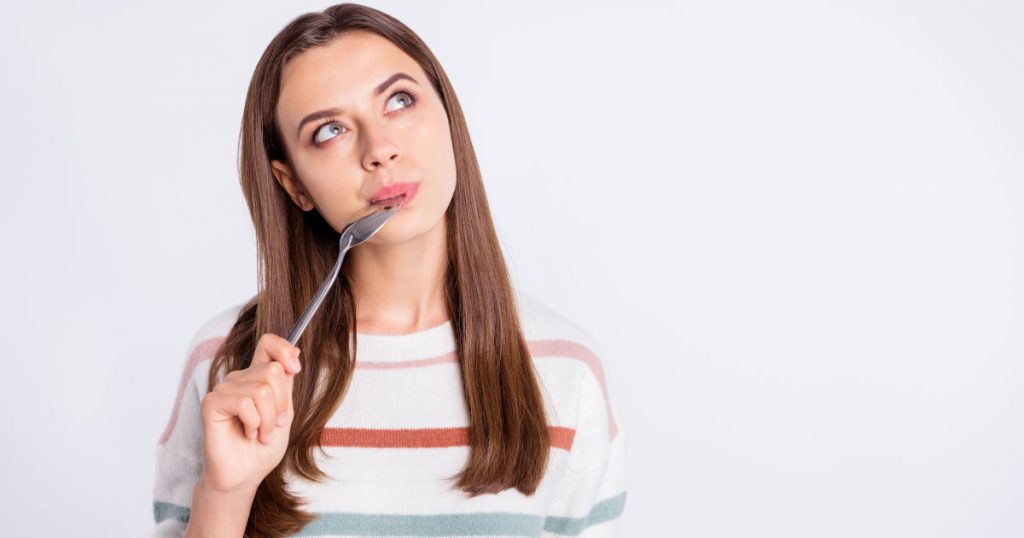 Eine junge Frau hat einen Löffel in ihrem Mund und schaut verlegen nach oben