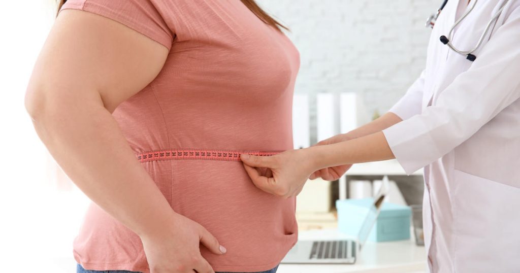 Eine Ärztin misst mit einem Maßband den Taillenumfang einer stark übergewichtigen Frau