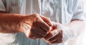 Eine ältere Frau hält ihre von Rheuma betroffenen Hände vor ihren Oberkörper.