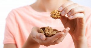 Eine Frau im rosa T-Shirt hält eine Hand voll Walnüsse in die Kamera. In der anderen hat sie eine, die sie essen möchte